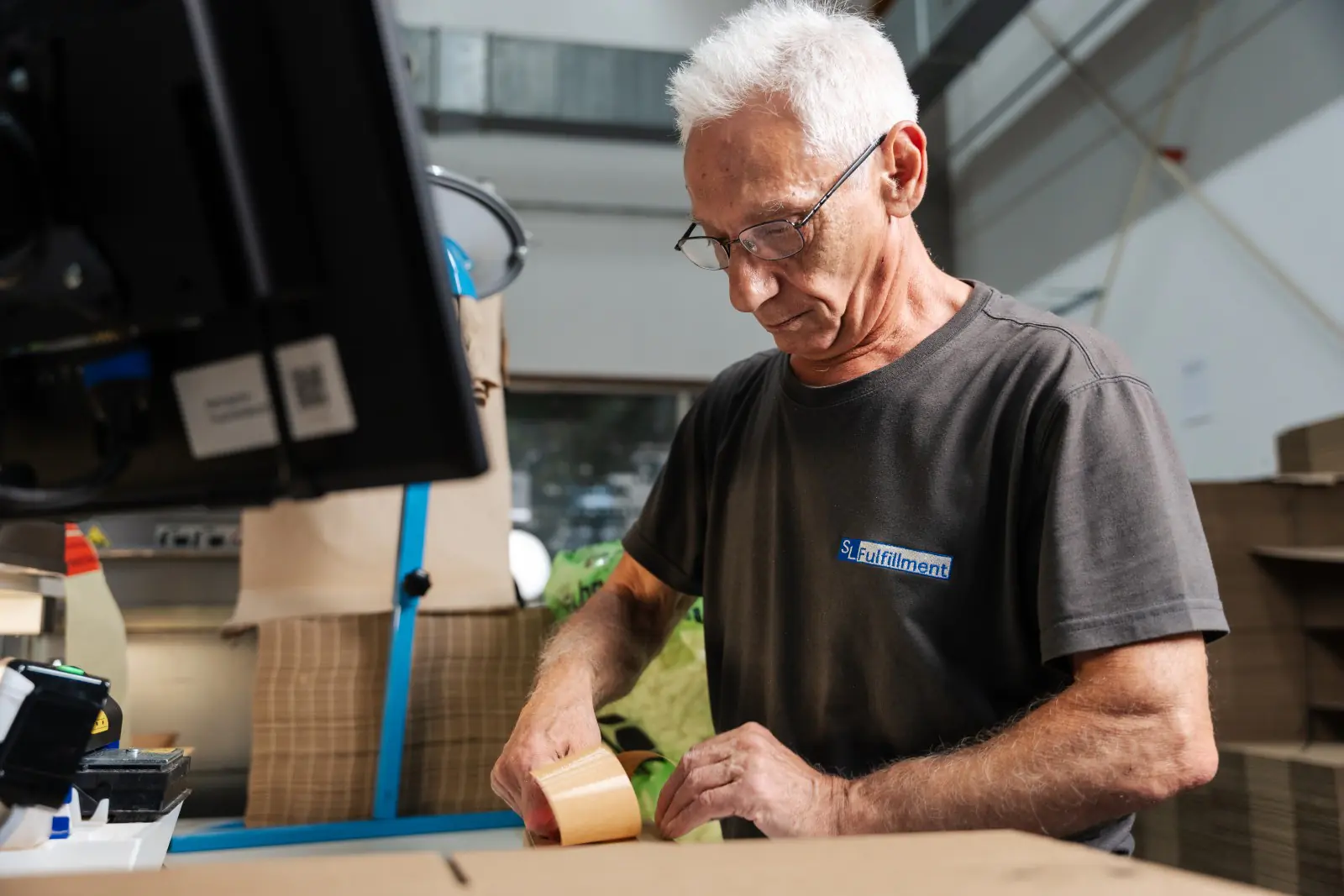 Mitarbeiter verpackt Bestellung am Packtisch im SL-Fulfillment Lager