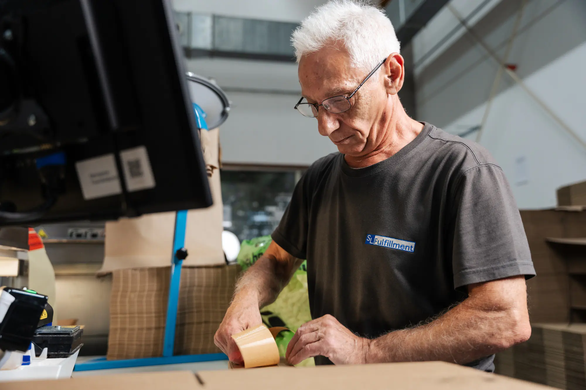 Mitarbeiter verpackt Bestellung am Packtisch im SL-Fulfillment Lager